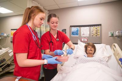 Nursing major students work with a human simulator mannequin.